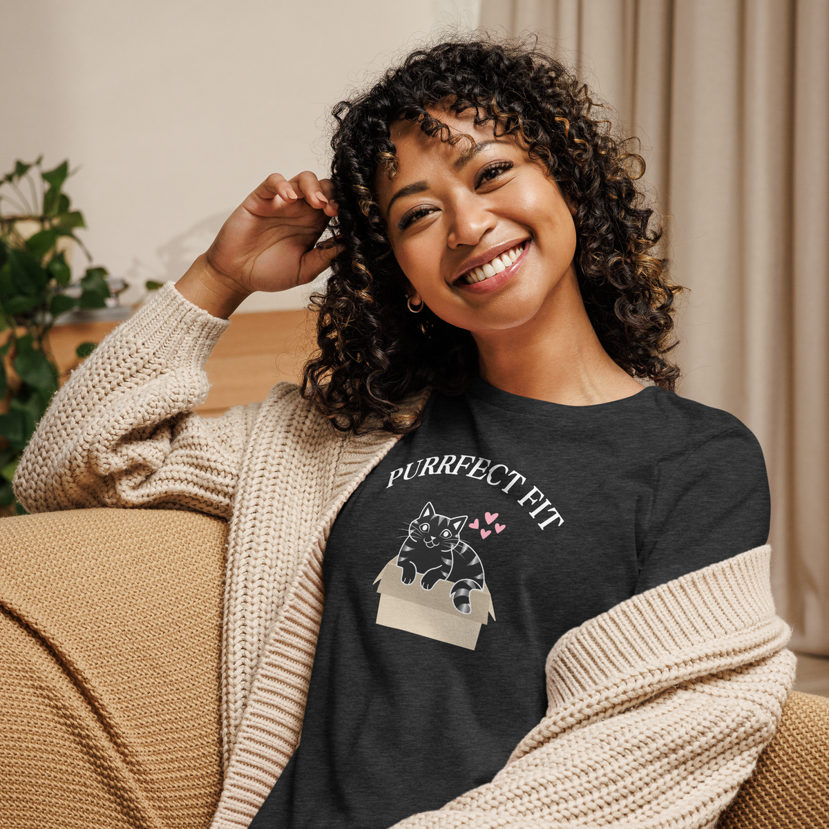 A smiling woman wearing a dark grey heather relaxed-fit t-shirt featuring a custom illustration of a cat inside a box with the arched text reading Purrfect Fit.